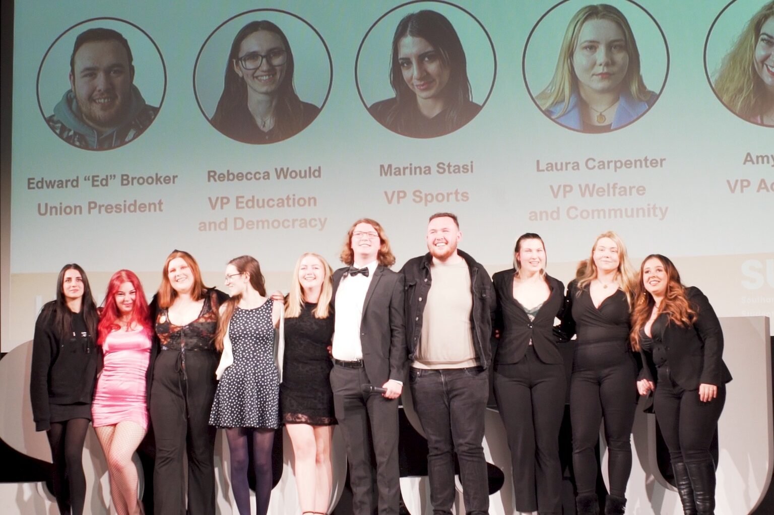 Elected sabatical officials smiling on stage with previous sabatical officers.